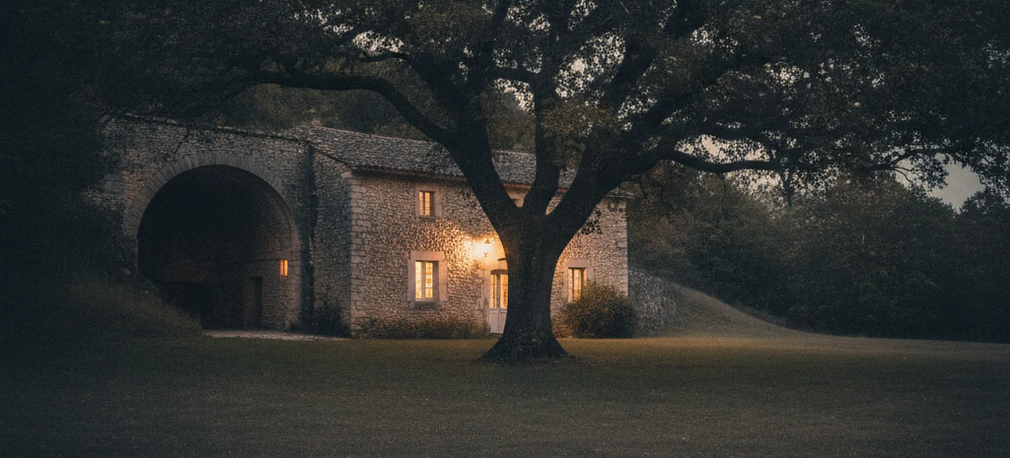 Grand chêne abritant une maison de pierre au crépuscule